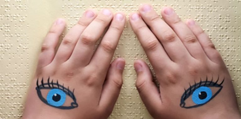 A child's hands with eyes drawn on them reading a braille page.