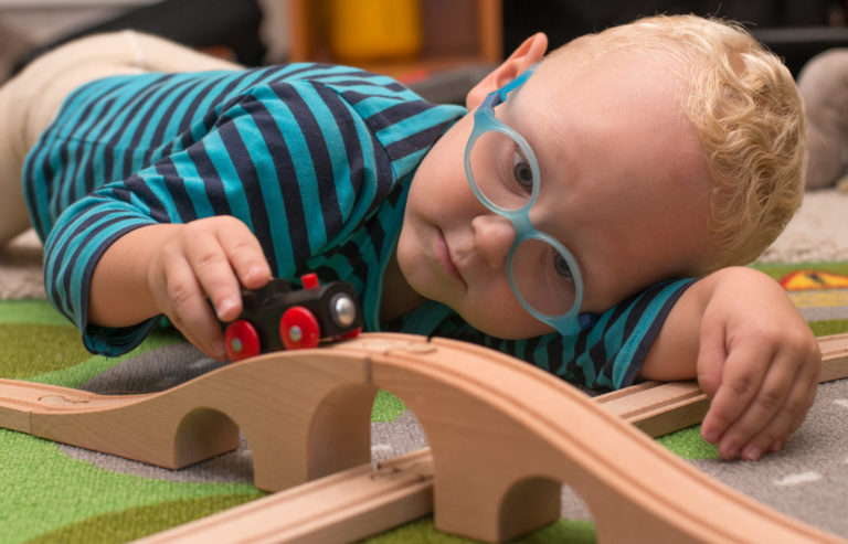 Little boy with glasses playing with a train on wooden tracks