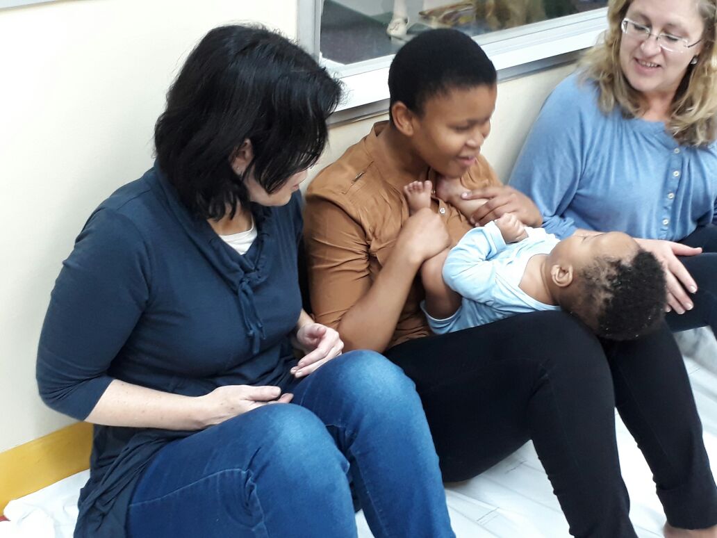 Mother holding baby on thighs so she can guide his hands to her face