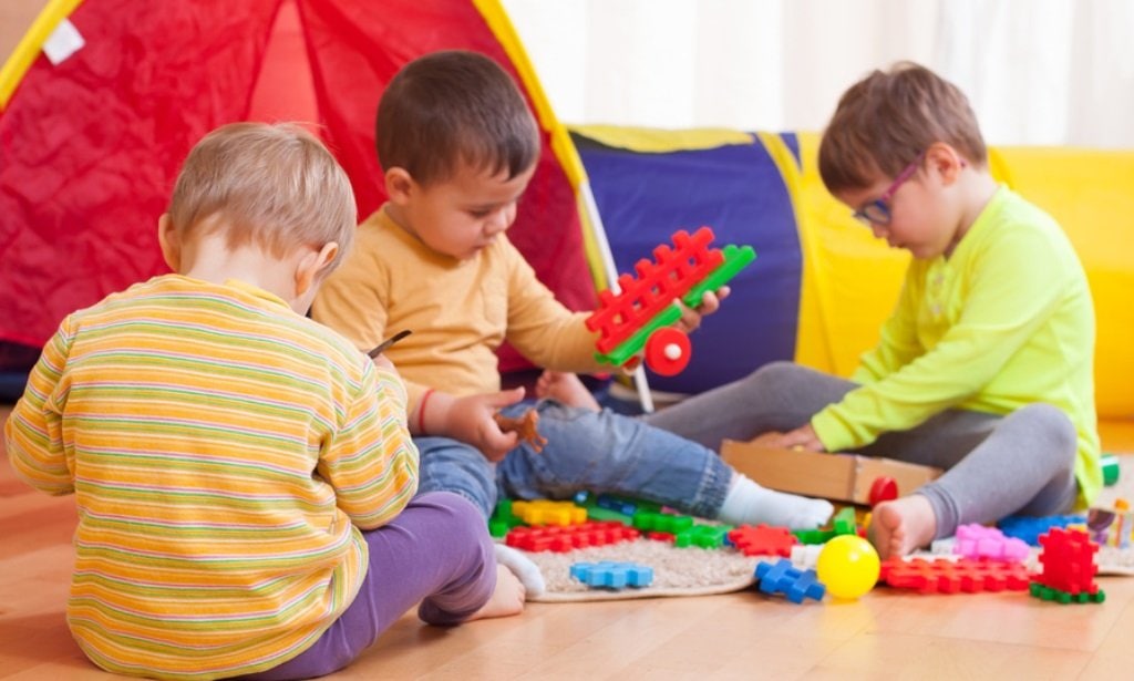 a group of three children playing on the floor with blocks