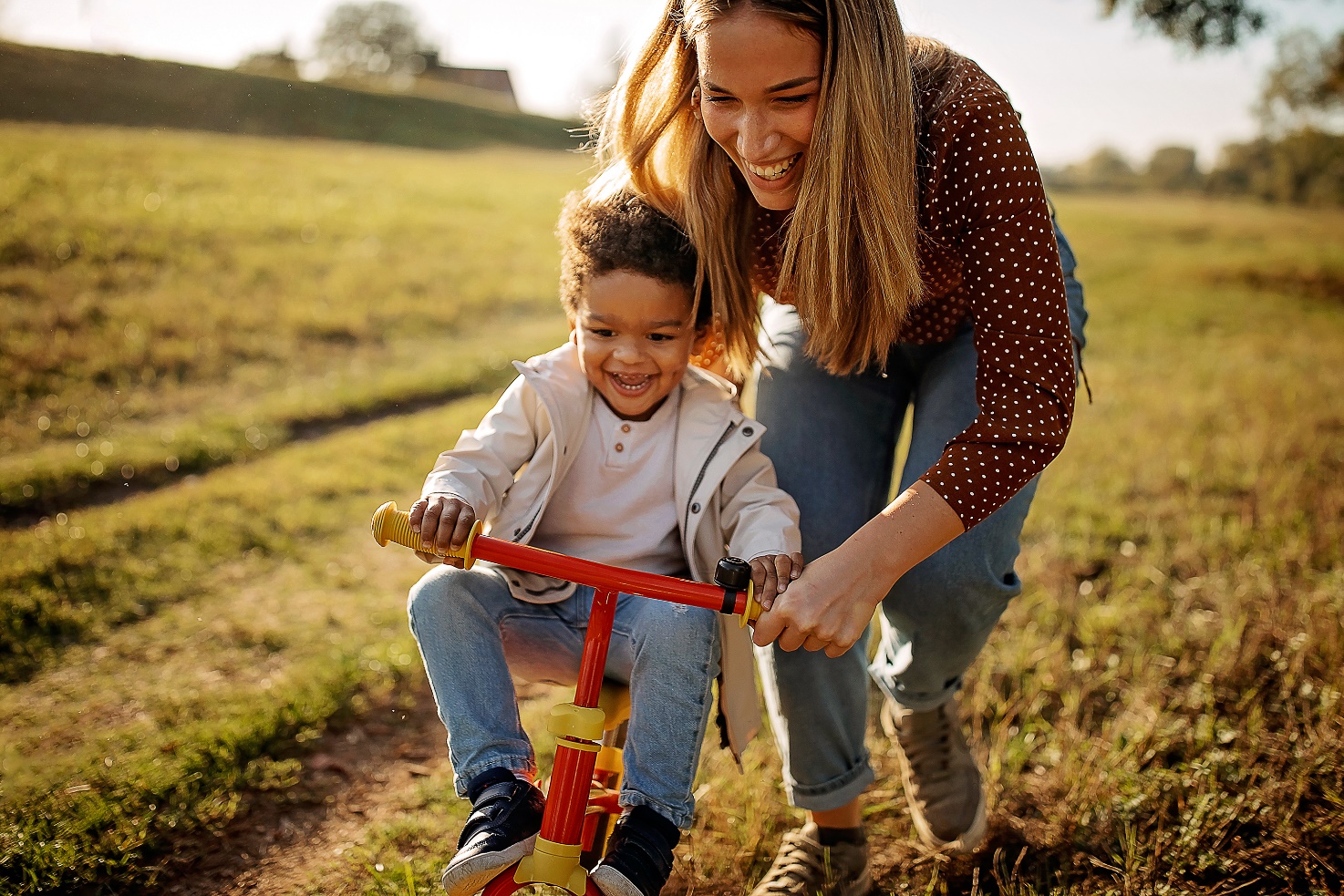 mother pushing child on bicycle on grass outdoors