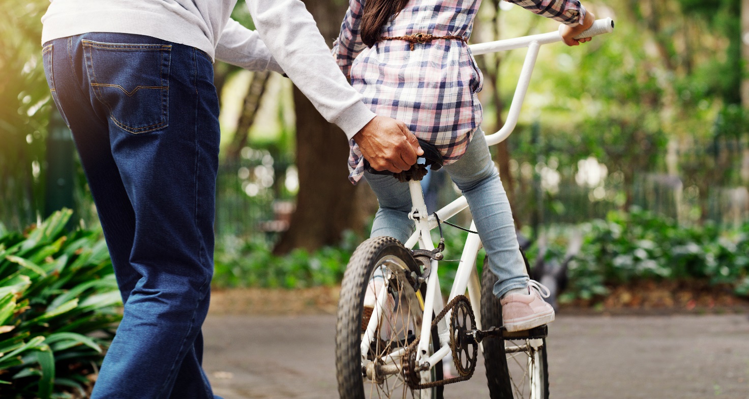 person teaching child to ride bicycle by holding the seat and running beside them