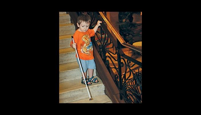 A visually impaired boy going down stairs with his white cane